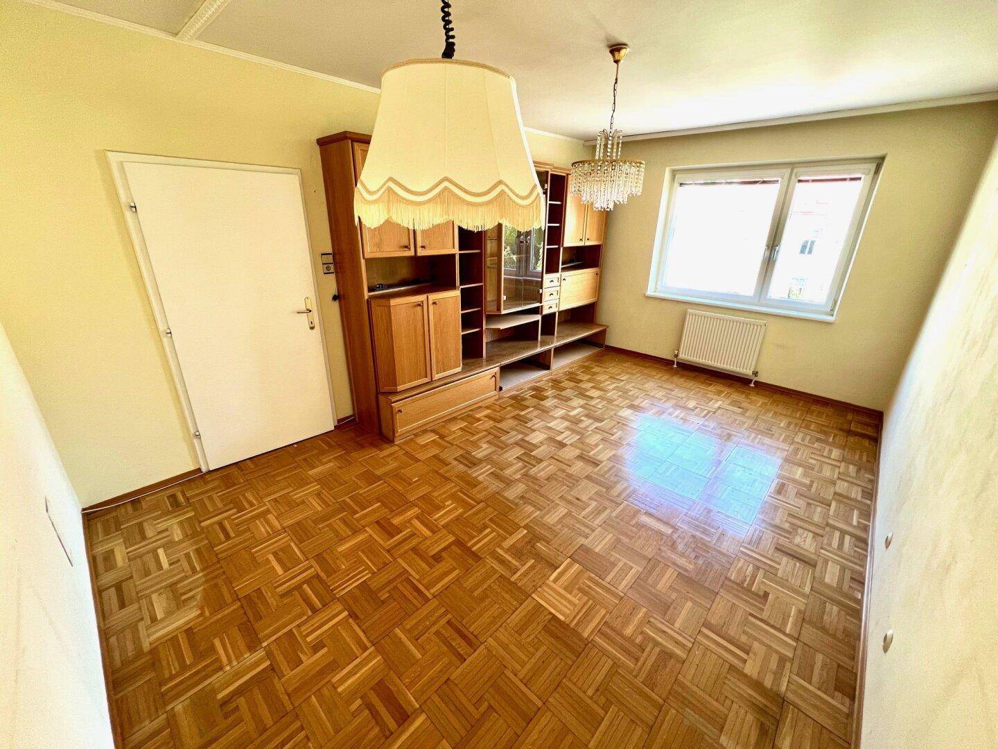 Wohnzimmer mit Parkettboden und einer großen Holzschrankwand, die viel Stauraum bietet.