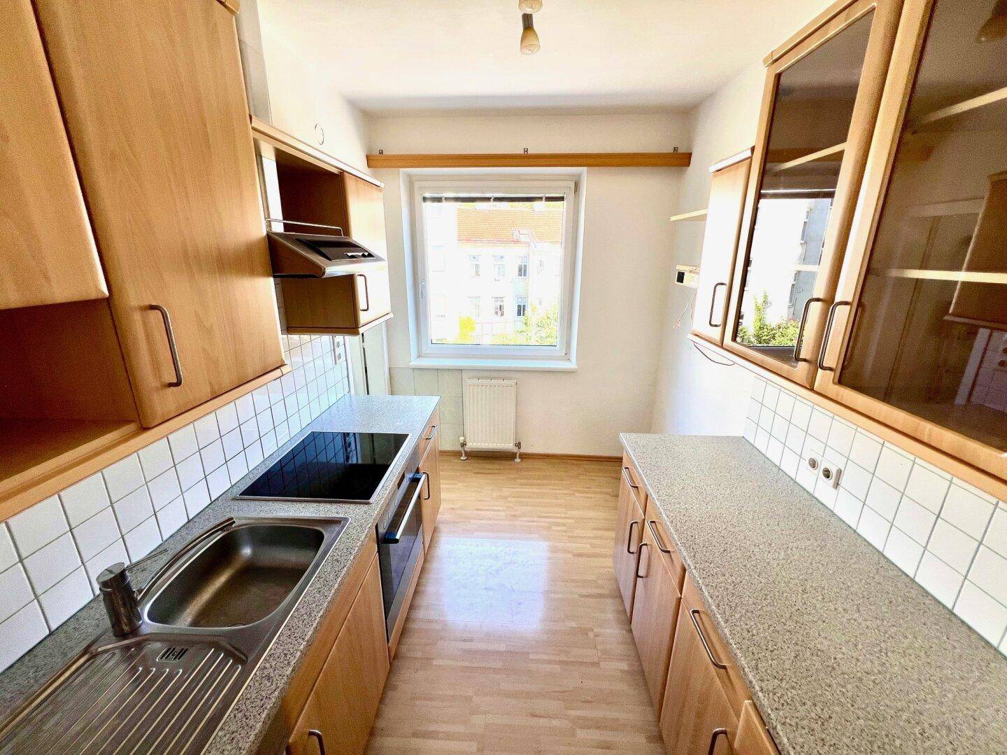 Funktionale Küche mit Holzschränken, Einbaugeräten und Fenster für Tageslicht.