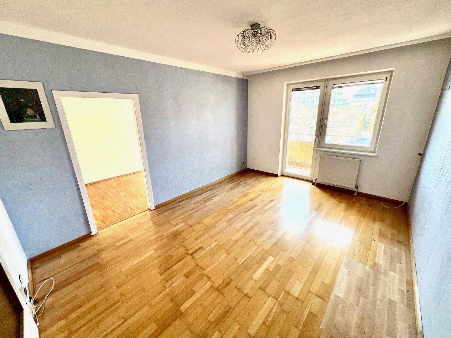 Geräumiges Zimmer mit Parkettboden und Zugang zu weiteren Räumen sowie einem Balkon.