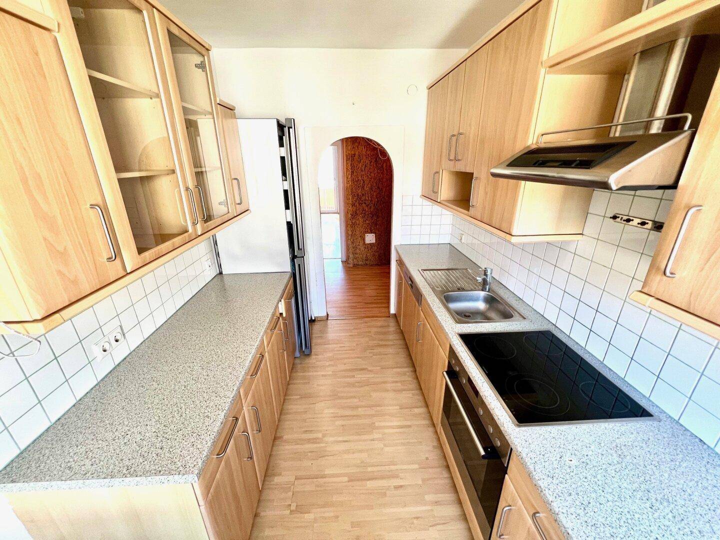 Längliche Küche mit Holzfronten, integrierten Geräten und ausreichend Arbeitsfläche.