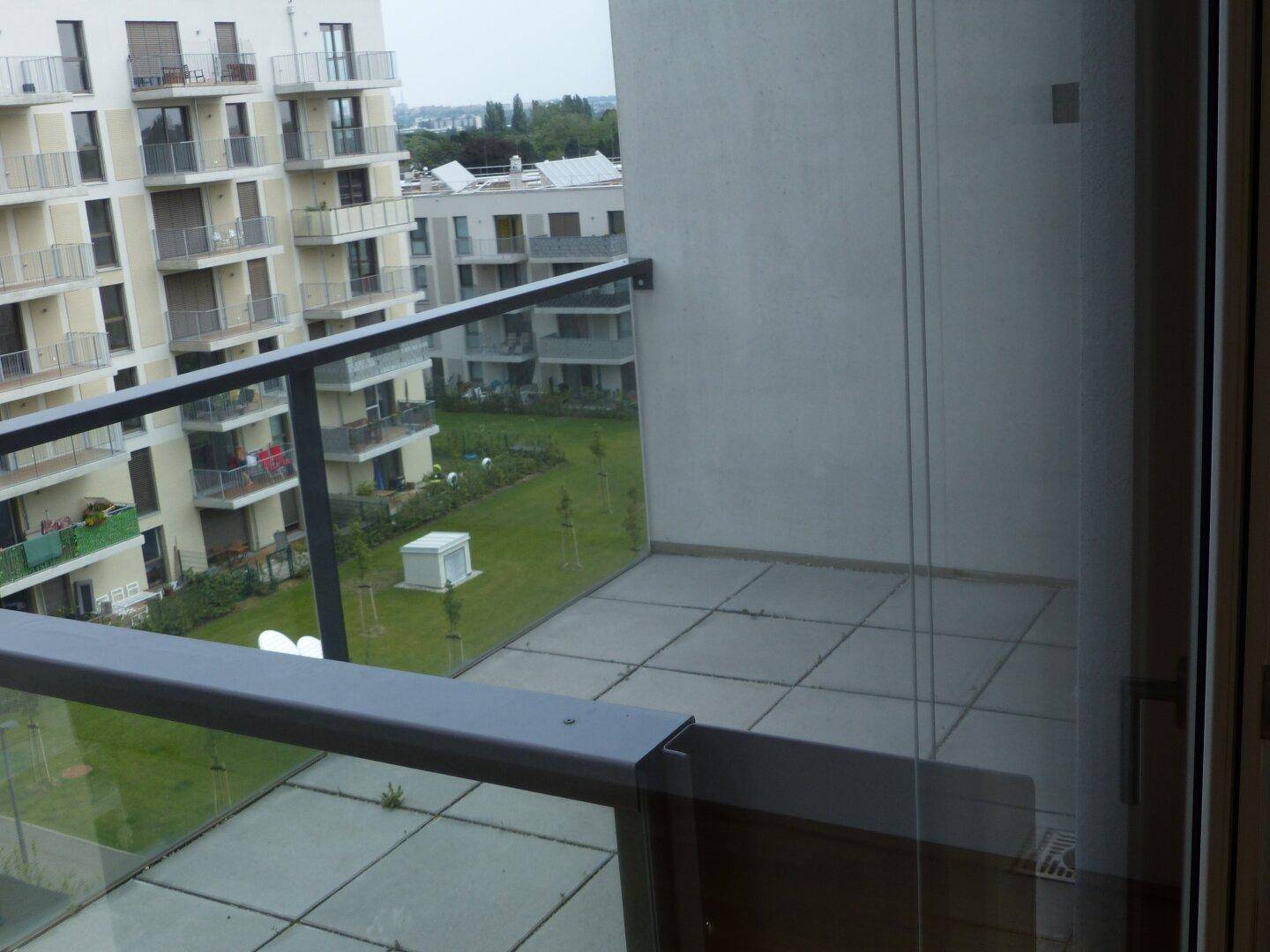 Balkon mit Fliesenboden und Blick auf die umliegenden Wohngebäude und Grünflächen.