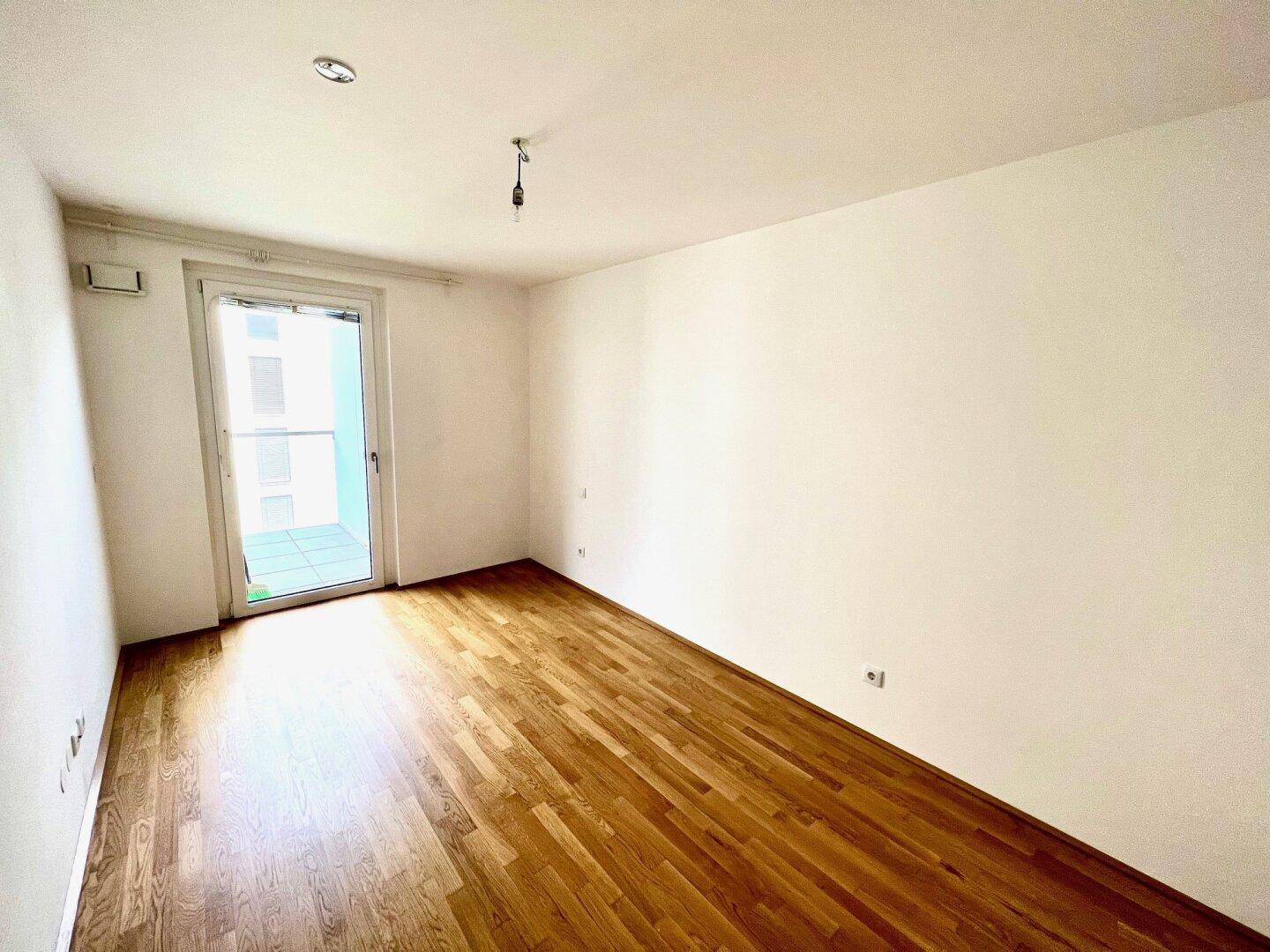 Helles Schlafzimmer mit Parkettboden und direktem Zugang zu einem Balkon.