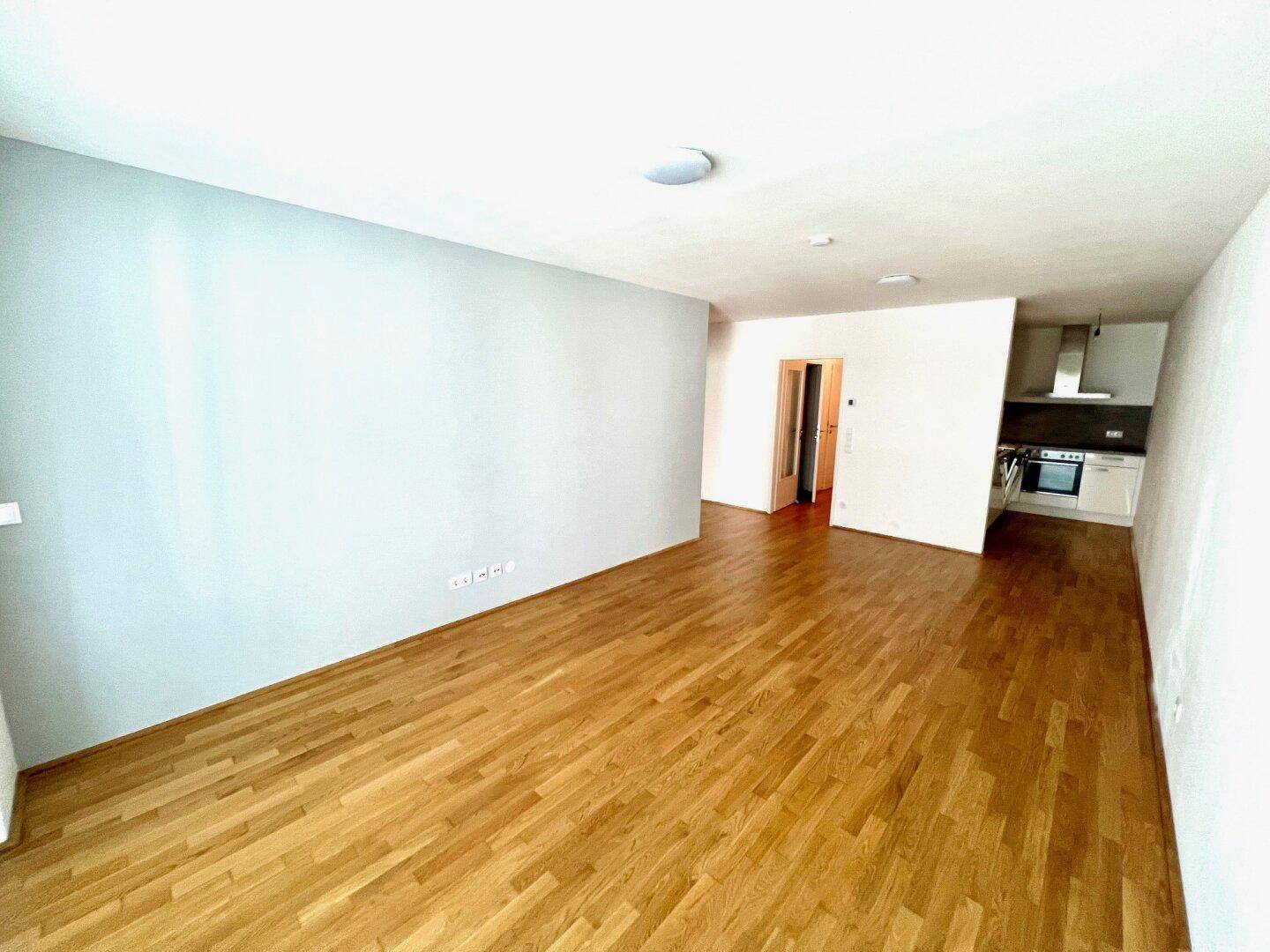Geräumiges Wohnzimmer mit Parkettboden und Blick auf den Küchenbereich.