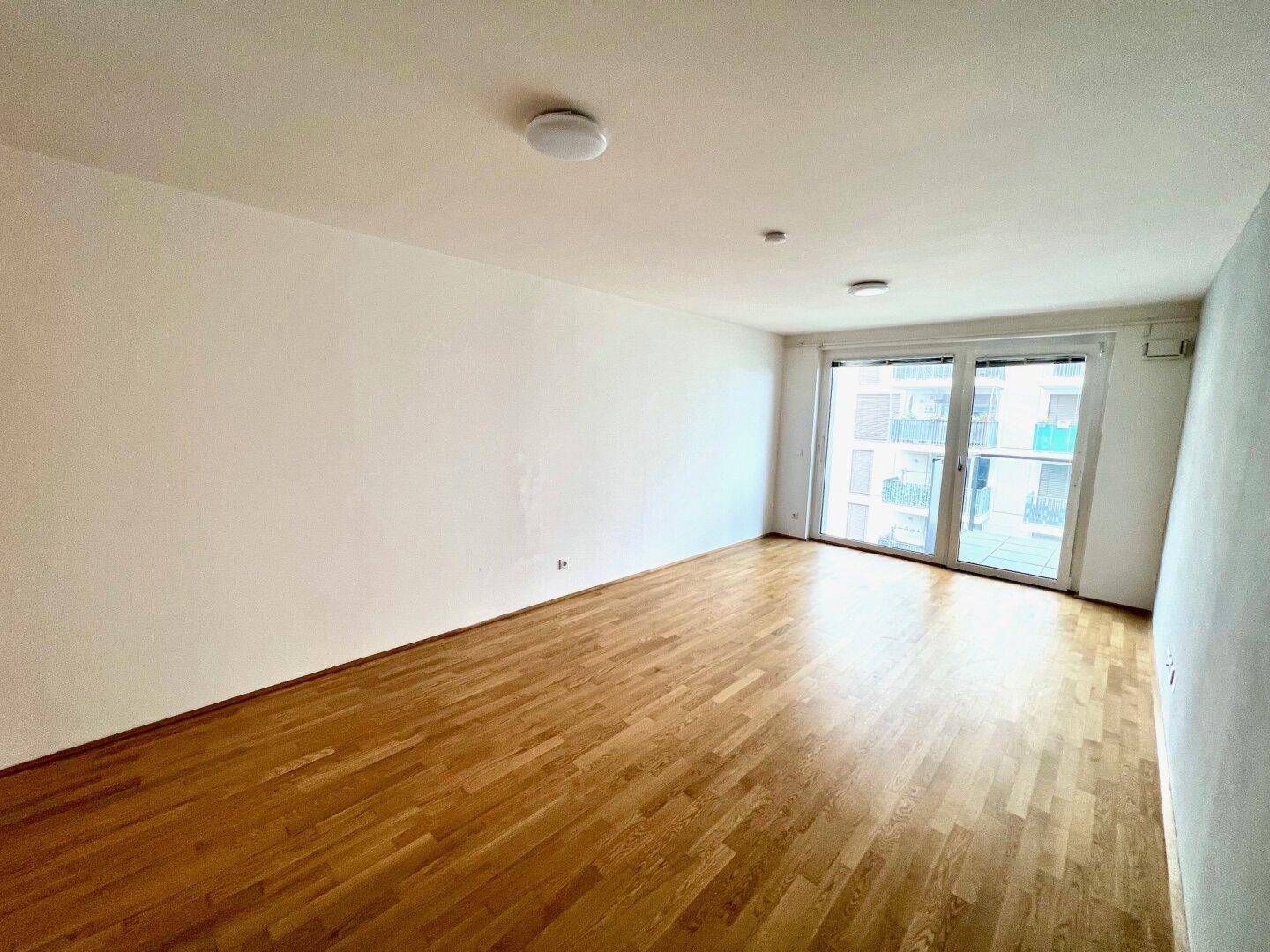 Lichtdurchflutetes Wohnzimmer mit Holzboden und großen Fenstern zum Balkon.