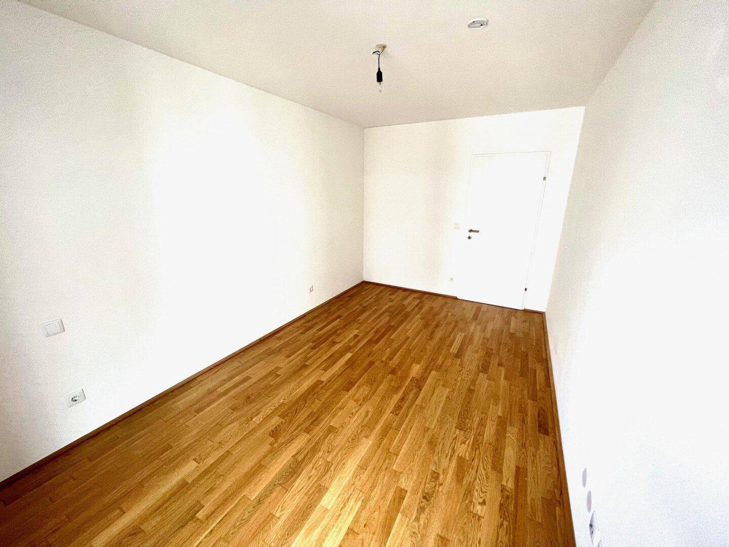 Leeres Schlafzimmer mit Holzboden und weißen Wänden, bereit zur individuellen Gestaltung.