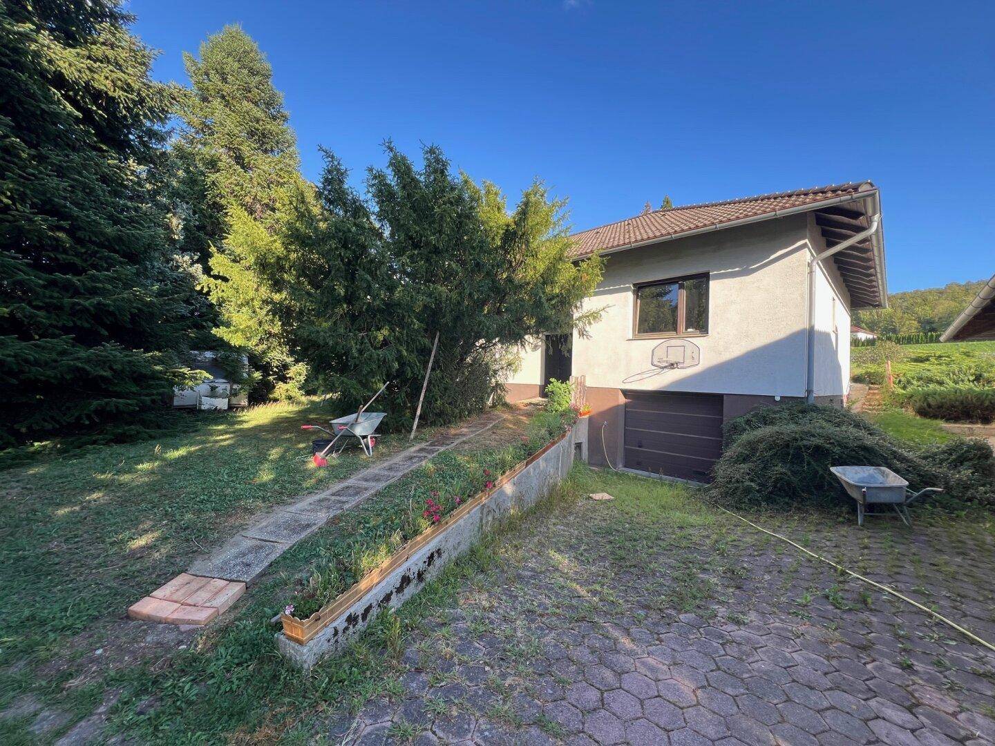 Vorderansicht des Hauses mit gepflasterter Auffahrt, integrierter Garage und Gartenbereich.
