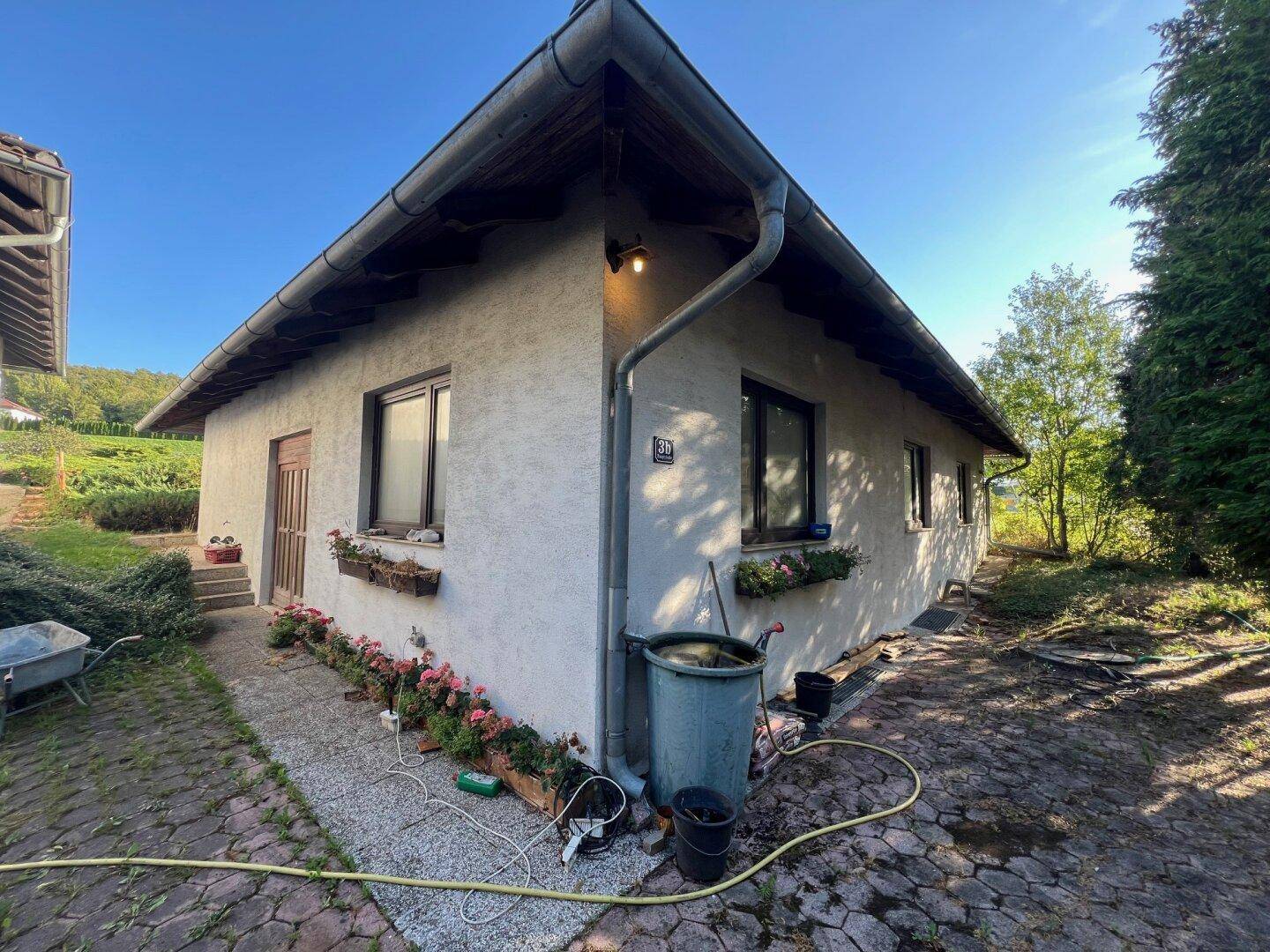 Ecke eines Hauses mit gepflastertem Weg, Blumenkästen an den Fenstern und Regenrinne.