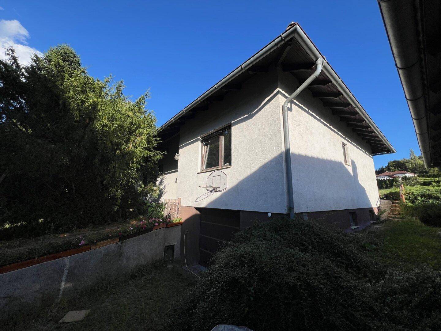 Seitenansicht des Hauses mit integrierter Garage, Basketballkorb und schattigem Gartenbereich.