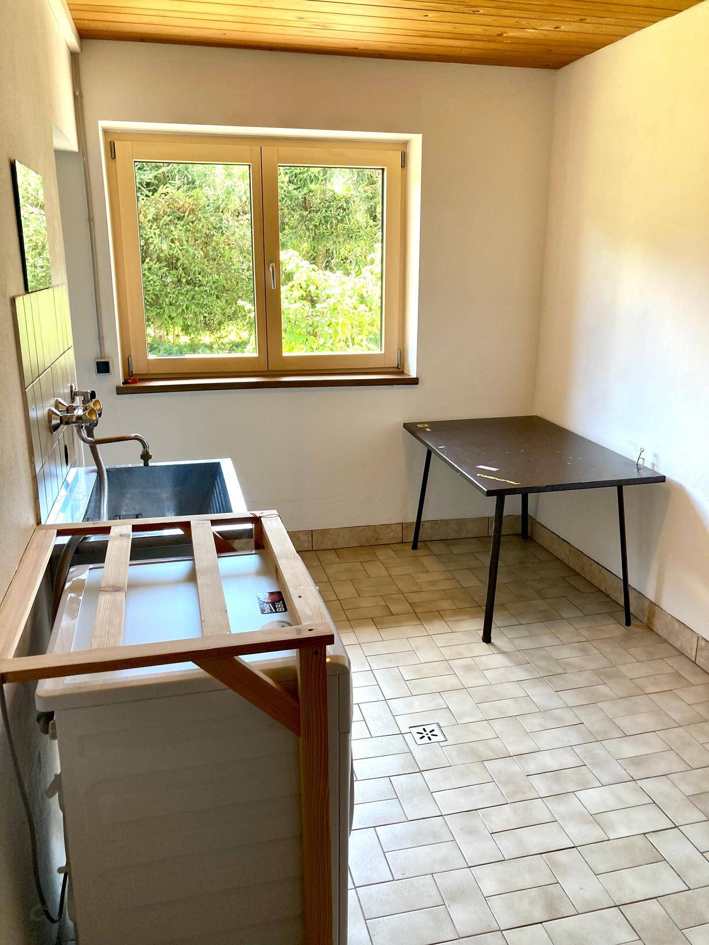 Hauswirtschaftsraum mit Waschbecken, Waschmaschine und Holzdielen-Decke, mit Fenster.