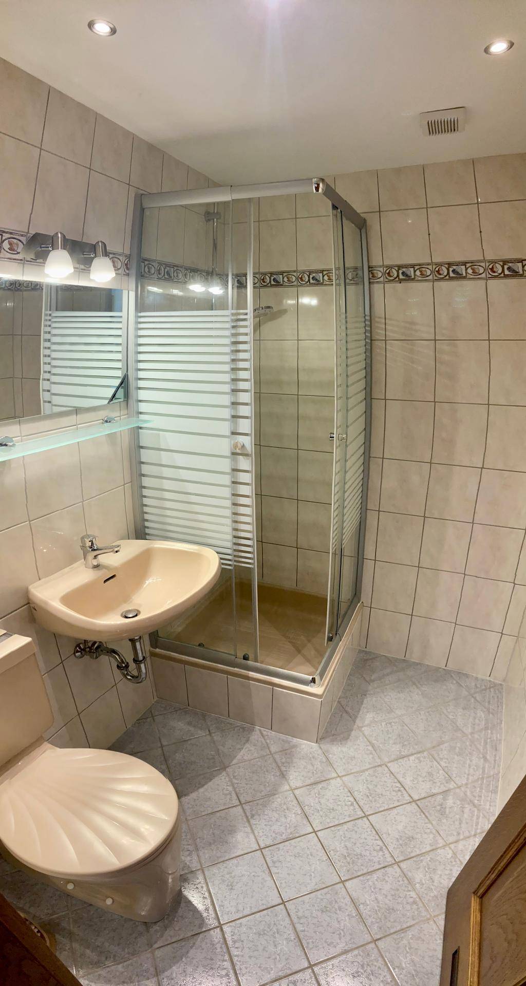 Gefliestes Badezimmer mit Dusche, WC und Waschbecken in hellen Farbtönen.