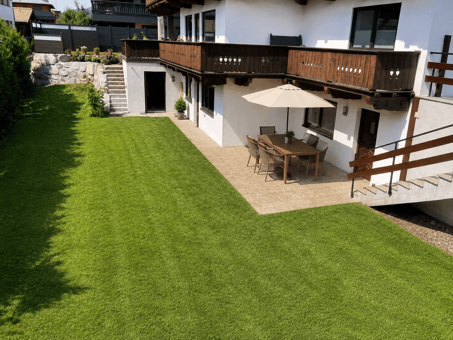Gepflegte Hausfassade im Chalet-Stil mit großem Rasen, möblierter Terrasse und Balkon.