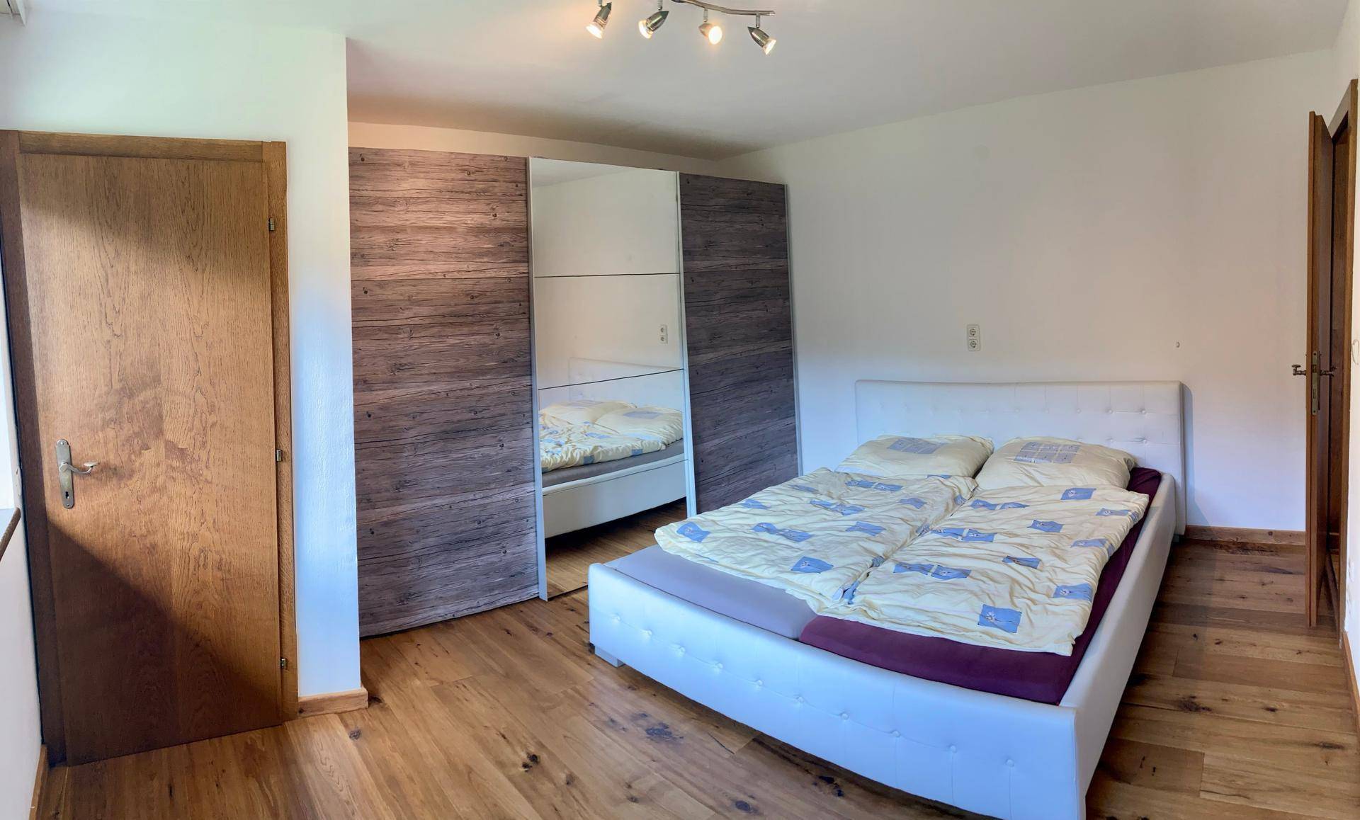 Schlafzimmer mit Doppelbett, Spiegelschrank und Holzboden, hell und funktional eingerichtet.
