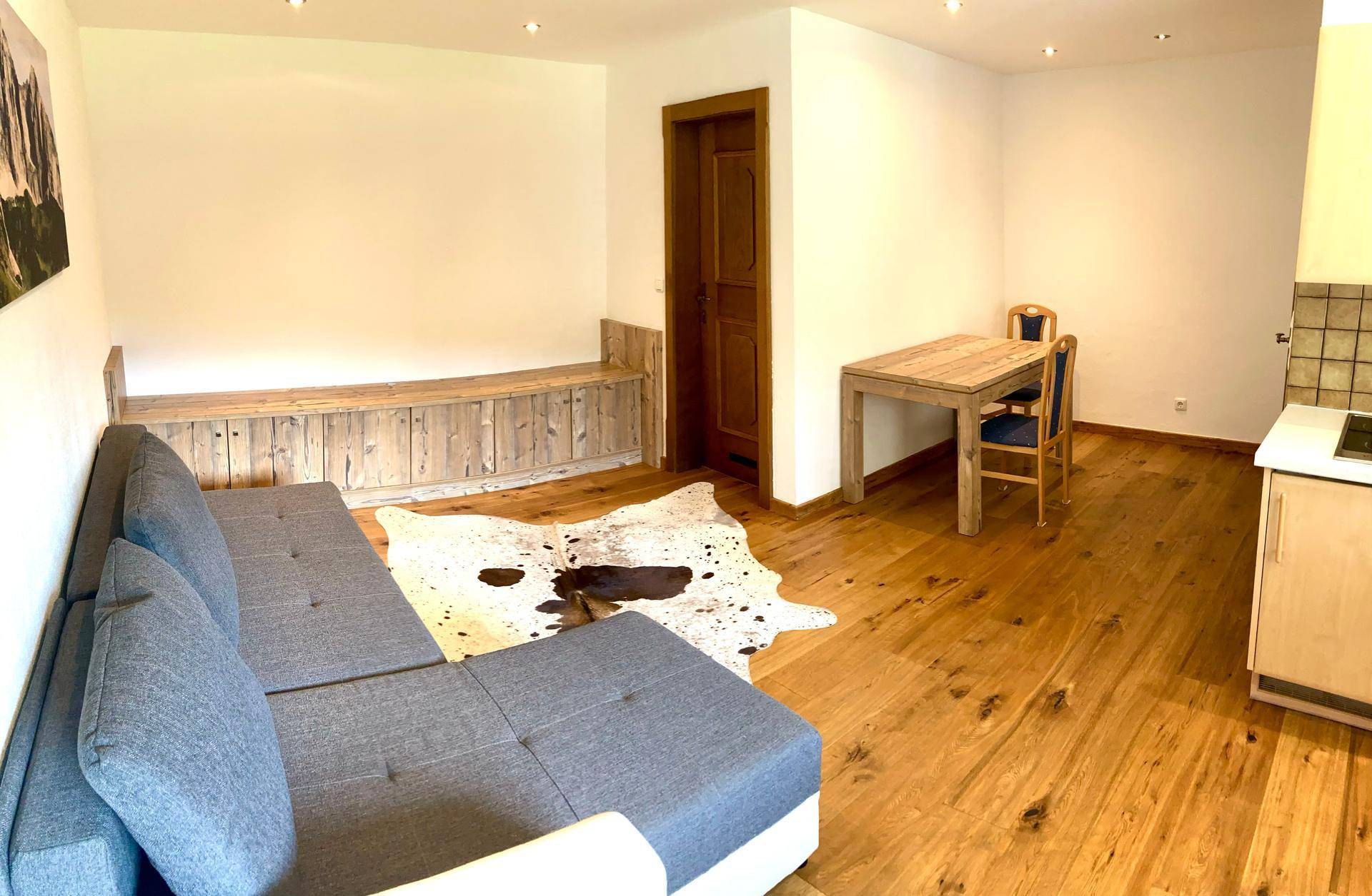 Wohn-Essbereich mit Holztisch, Sofa und rustikaler Holzbank, kombiniert mit Küchenzeile.