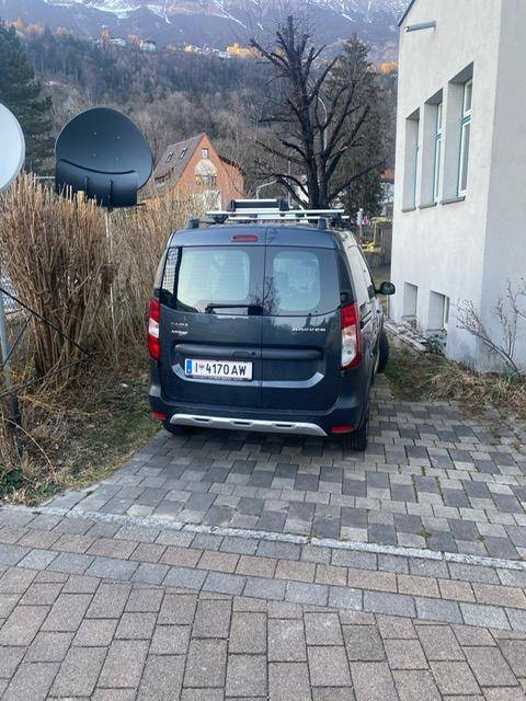 Ein geparktes Fahrzeug auf einem gepflasterten Stellplatz neben einem Gebäude mit Bergblick im Hintergrund.