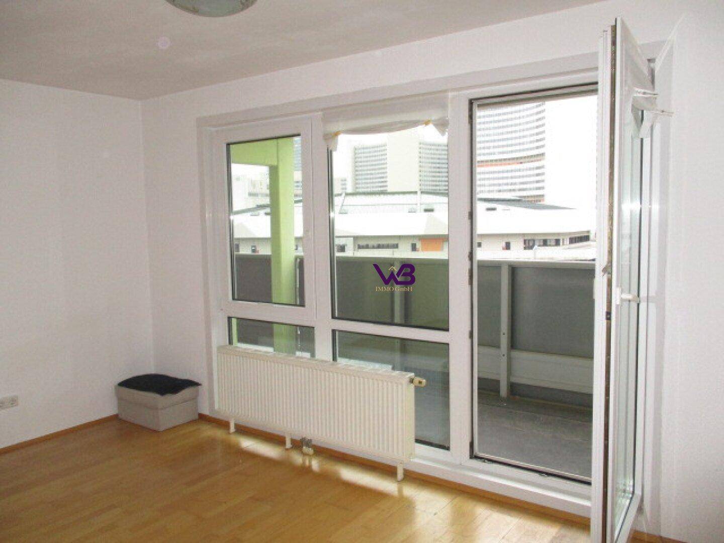 Heller Raum mit Parkettboden und großen Fenstern, die Zugang zu einem Balkon bieten.