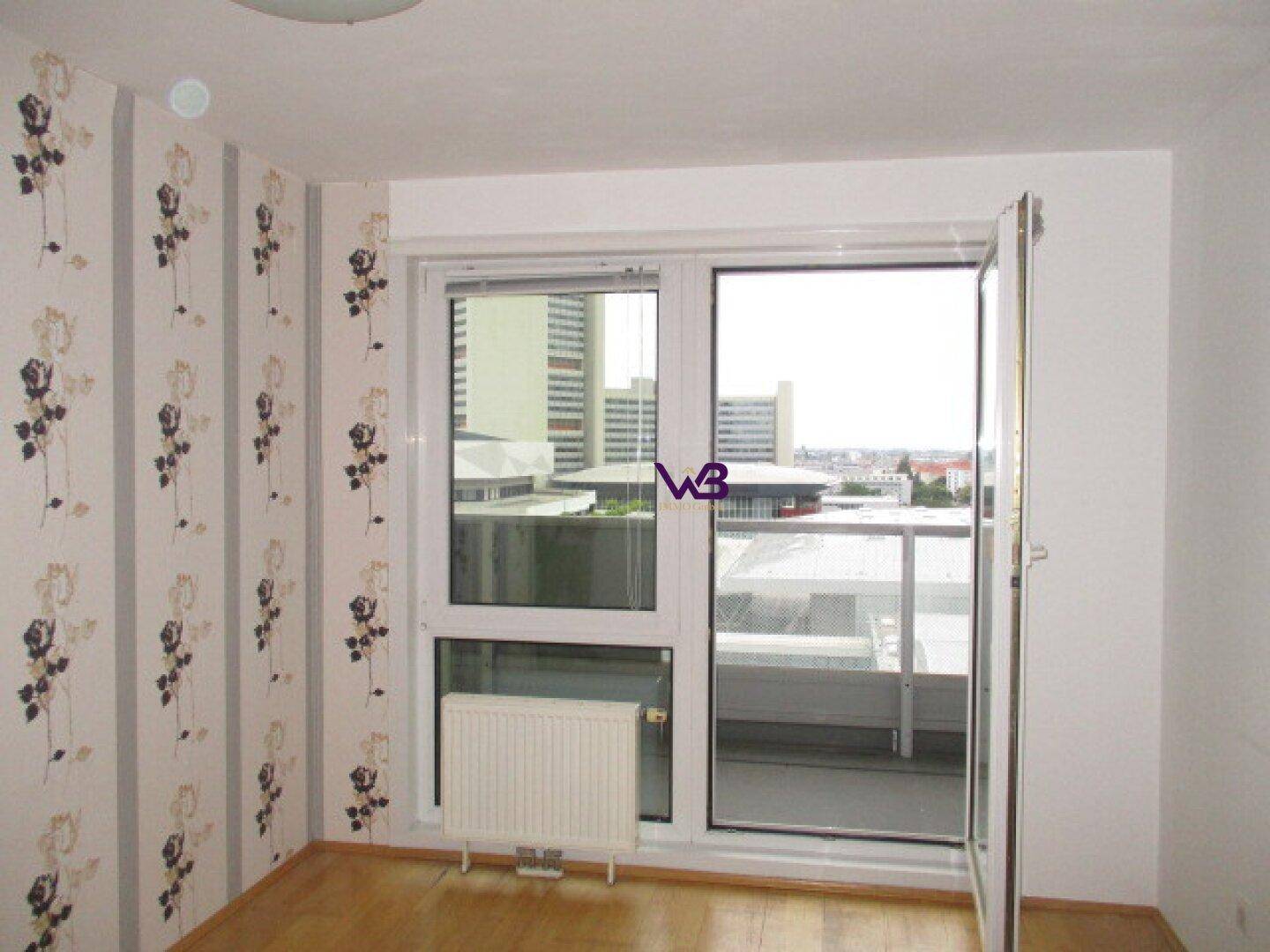 Schlafzimmer mit floraler Tapete, Parkettboden und Zugang zu einem Balkon.