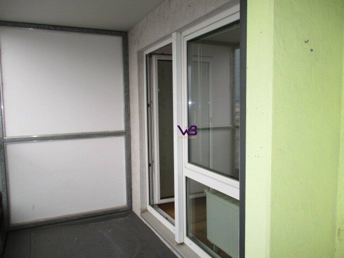 Balkon mit hellgrüner Wand und Zugang zum Innenraum durch eine Glastür.