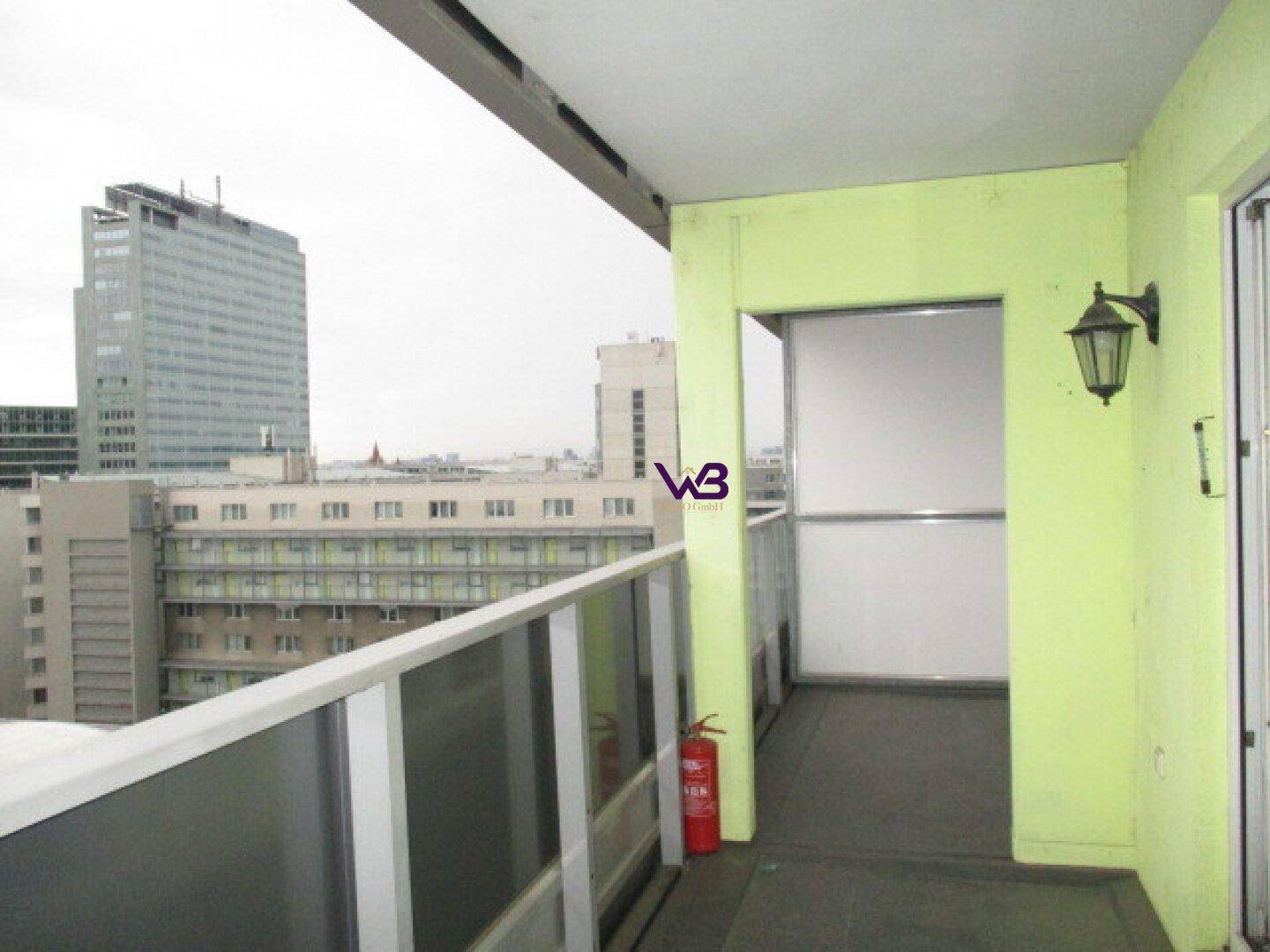 Balkon mit hellgrünen Wänden, Glasgeländer und Blick auf die Stadt.