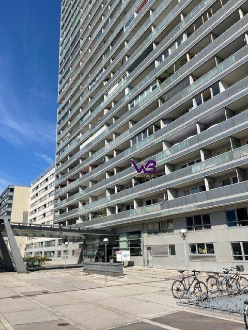 Hohes Wohngebäude mit vielen Balkonen und Fahrradständern im urbanen Umfeld.