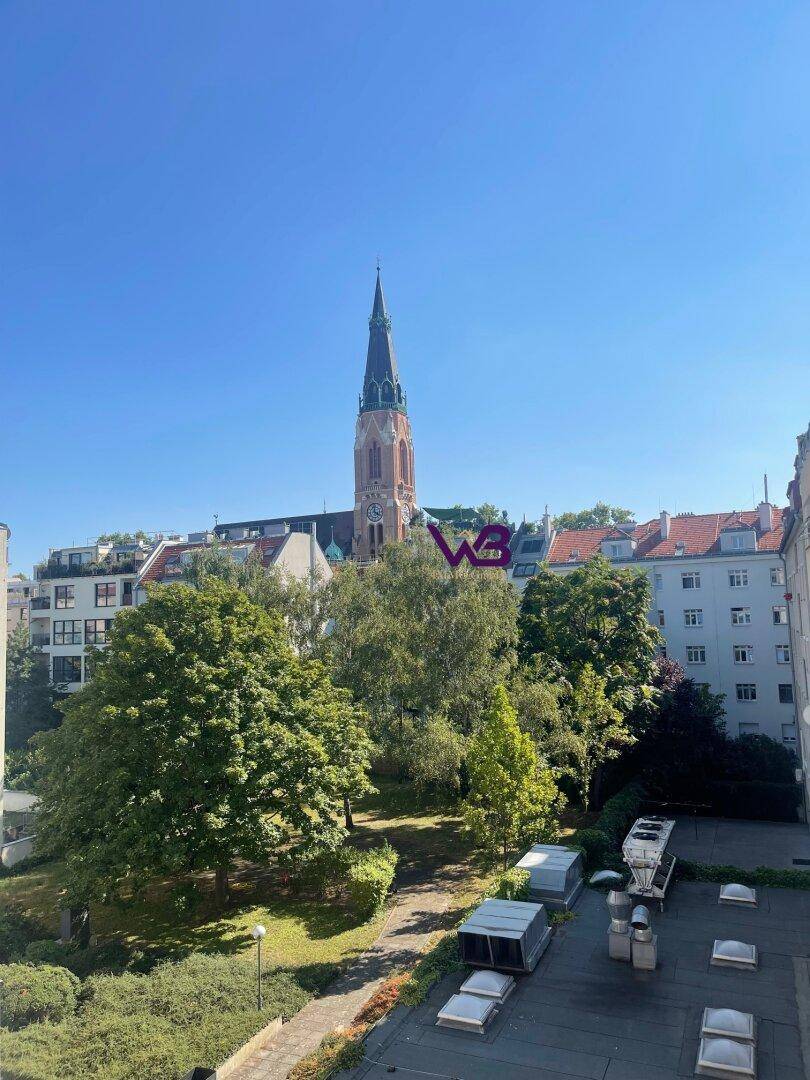 Blick von einem oberen Stockwerk auf eine Kirche, Bäume und umliegende Gebäude.