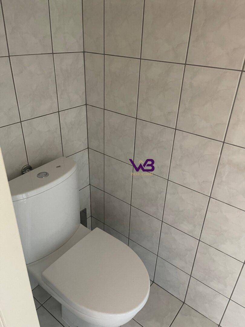 Separates WC mit Toilette und hellen Fliesen an den Wänden.