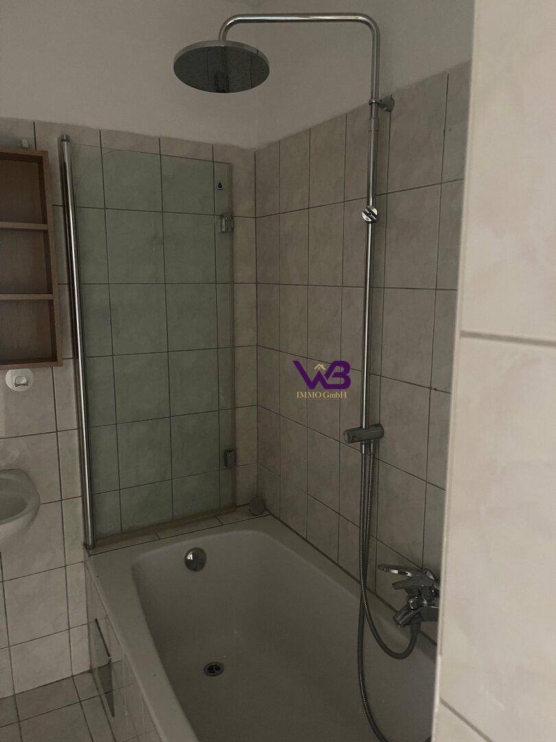 Badezimmer mit Badewanne, integrierter Dusche und hellen, funktionalen Fliesen.