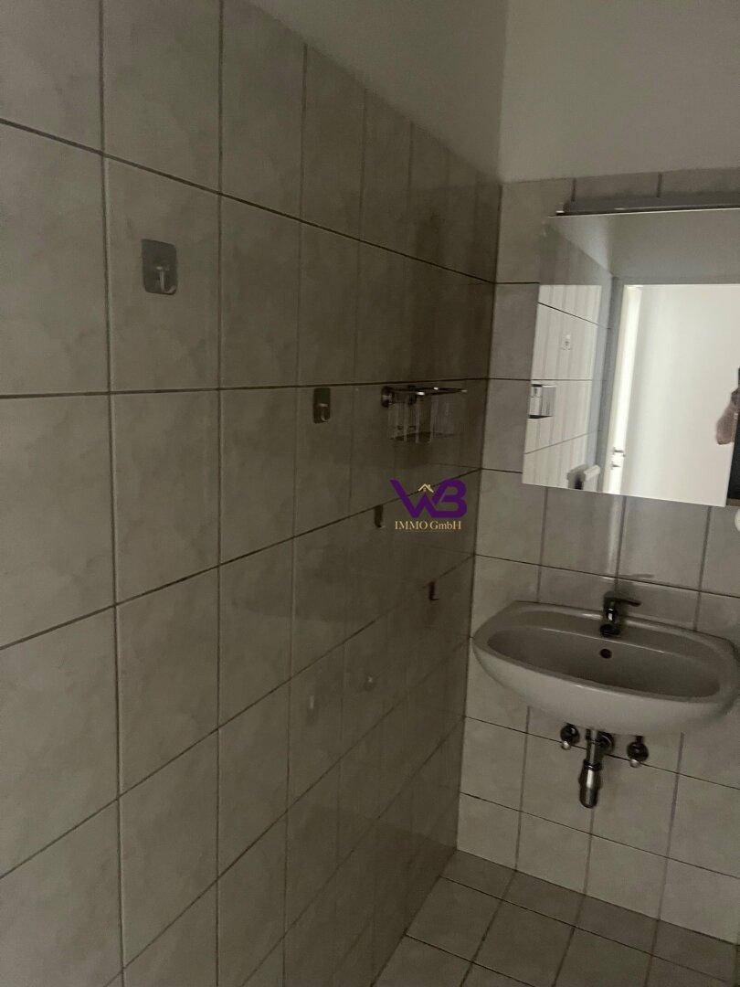 Gefliestes Badezimmer mit Waschbecken, Spiegel und einfacher Ausstattung.