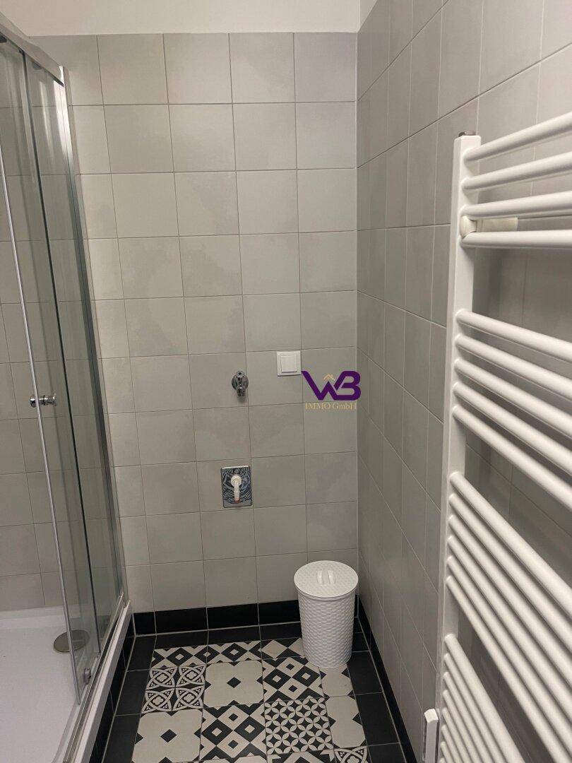 Badezimmerbereich mit grauen Wandfliesen, gemustertem Boden und einem weißen Handtuchheizkörper.