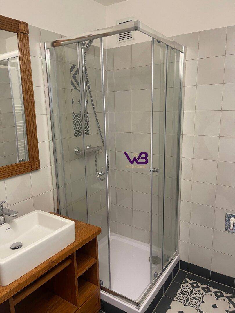 Modernes Badezimmer mit Duschkabine, Waschbecken auf Holzunterschrank und gemusterten Fliesen.