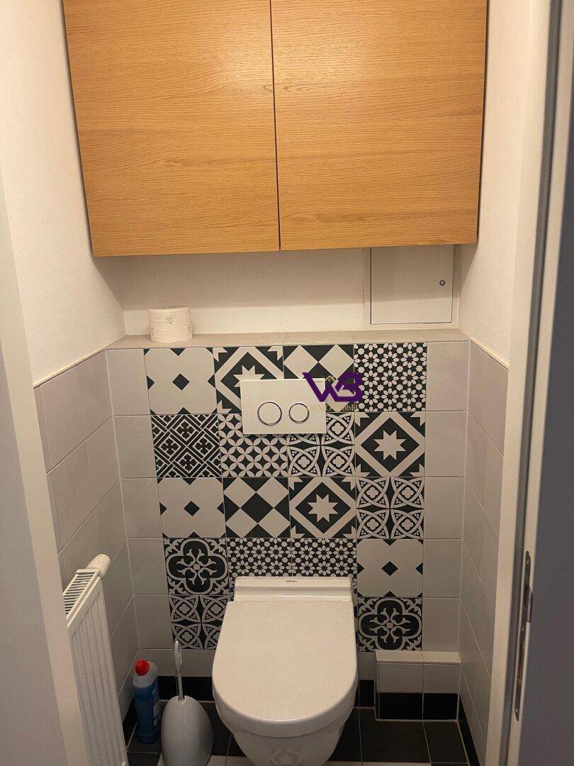 Separate Toilette mit Wand-WC, gemusterten Fliesen und einem Holzschrank über der Spülung.