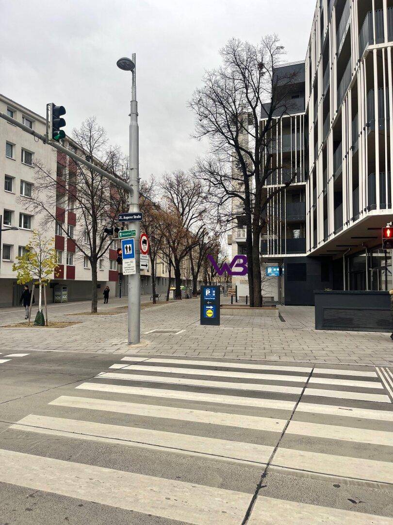 Stadtansicht mit Zebrastreifen, modernen Gebäuden und Bäumen an einer belebten Straße.