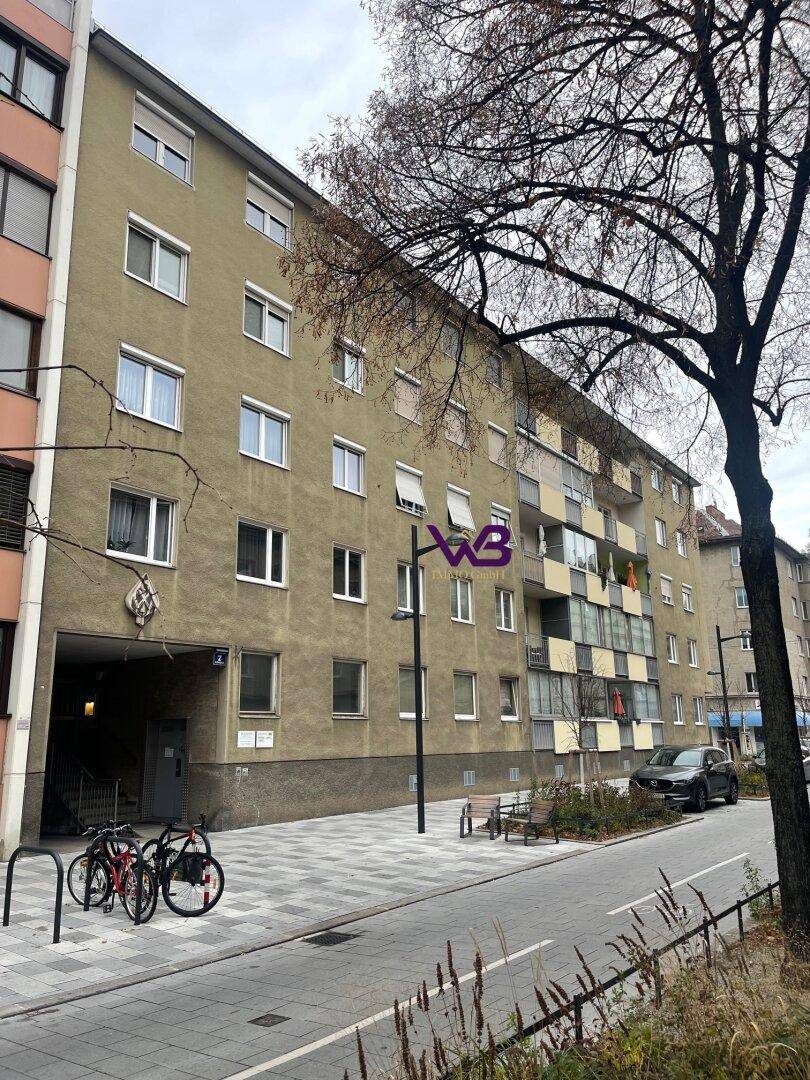 Fassade eines Mehrfamilienhauses mit mehreren Stockwerken und Fahrrädern vor dem Eingang.
