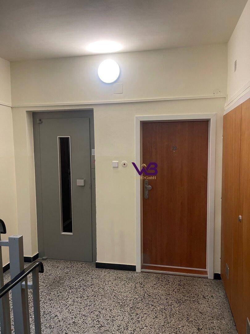 Heller Hausflur mit Aufzugstür, Wohnungstür und Terrazzoboden.