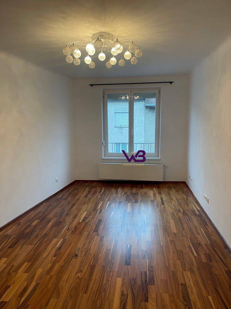 Geräumiges Zimmer mit elegantem Parkettboden, großen Fenstern und moderner Deckenleuchte.