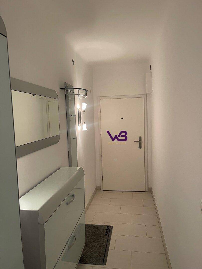 Heller Eingangsbereich mit Fliesenboden, Schuhschrank, Spiegel und moderner Beleuchtung.