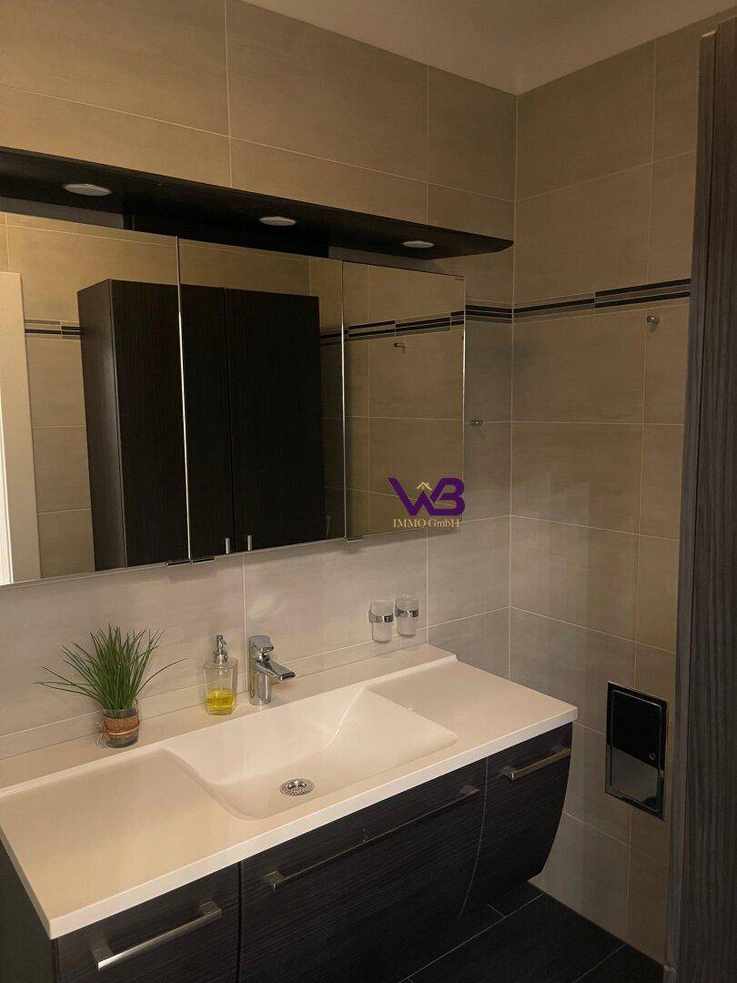 Modernes Badezimmer mit Waschtisch, Spiegelschrank und hellen Fliesen an den Wänden.