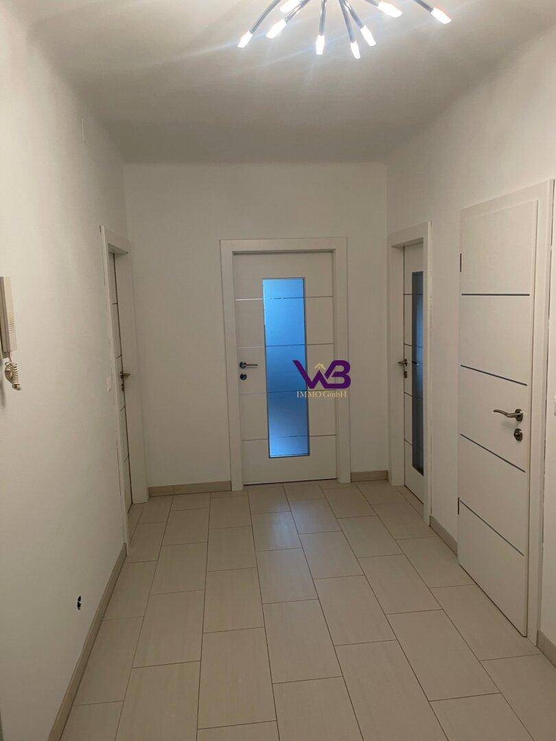 Heller Flur mit mehreren Türen, Fliesenboden und moderner Deckenbeleuchtung.