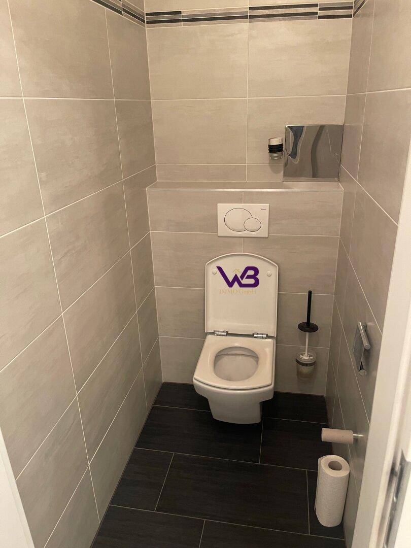 Separates WC mit wandhängender Toilette, Spülkasten und modernen Fliesen.