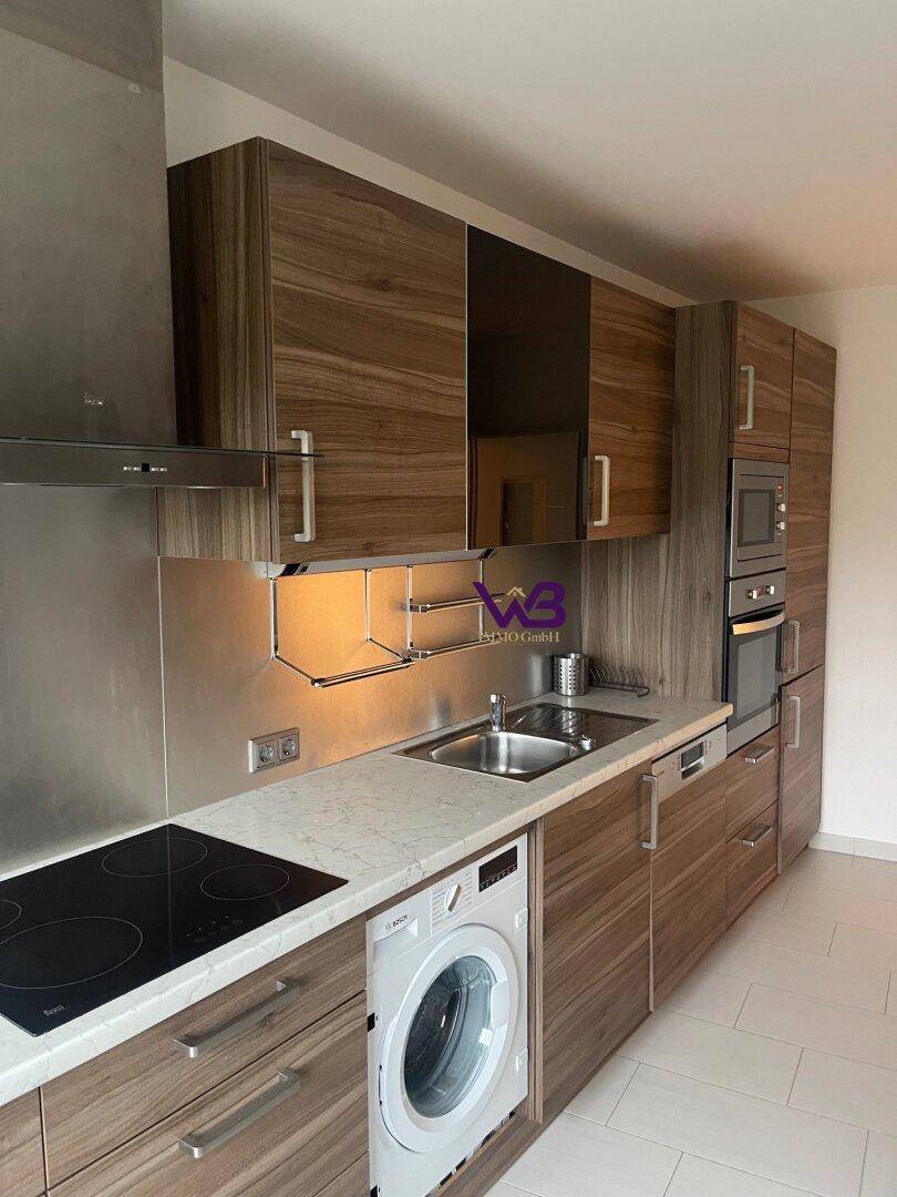 Moderne Küche mit Holzoptik-Schränken, integrierten Geräten und einer Waschmaschine unter der Arbeitsplatte.