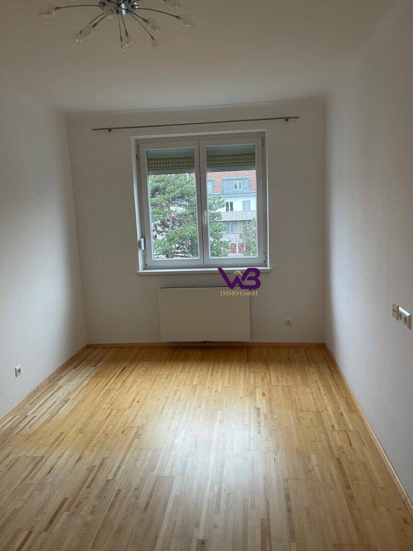 Helles Zimmer mit hellem Parkettboden, Fenster und Heizkörper darunter.