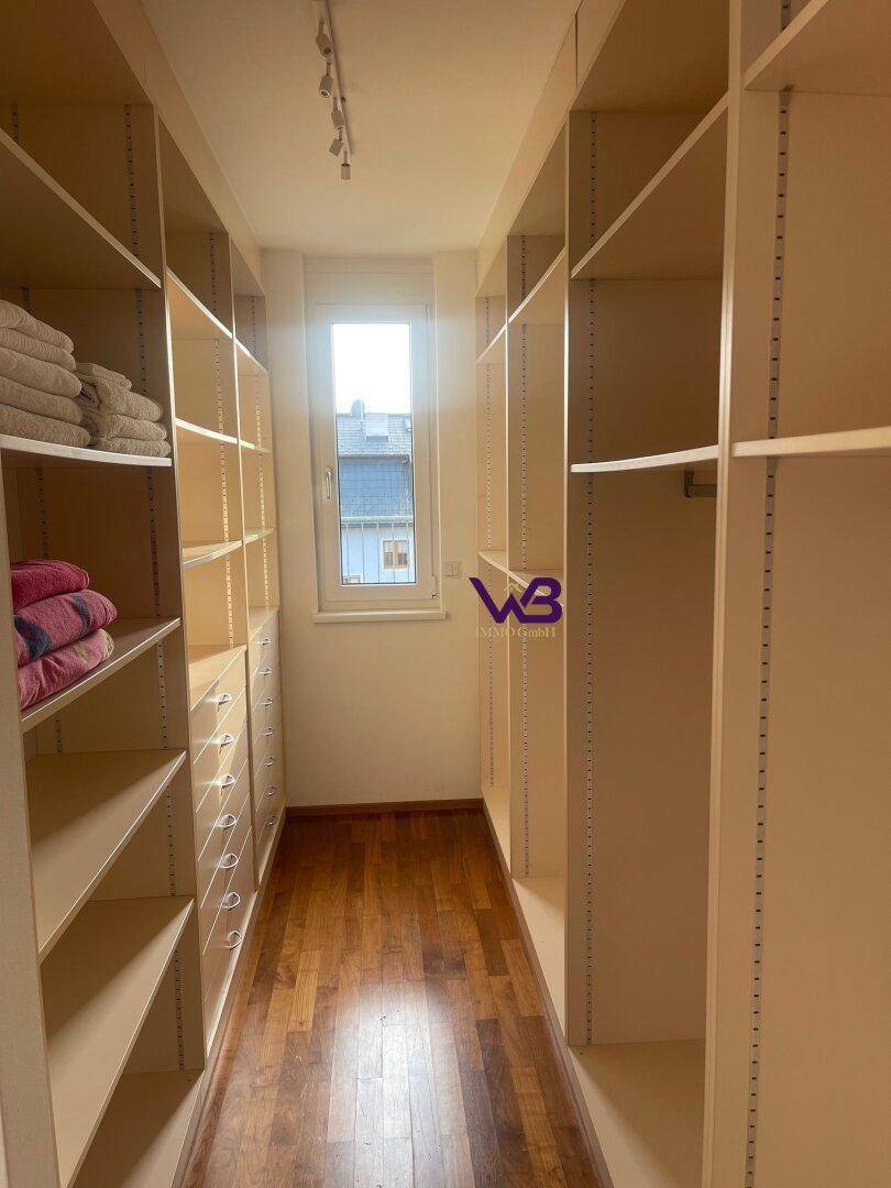 Geräumiger begehbarer Kleiderschrank mit vielen Regalen, Schubladen und Fenster.