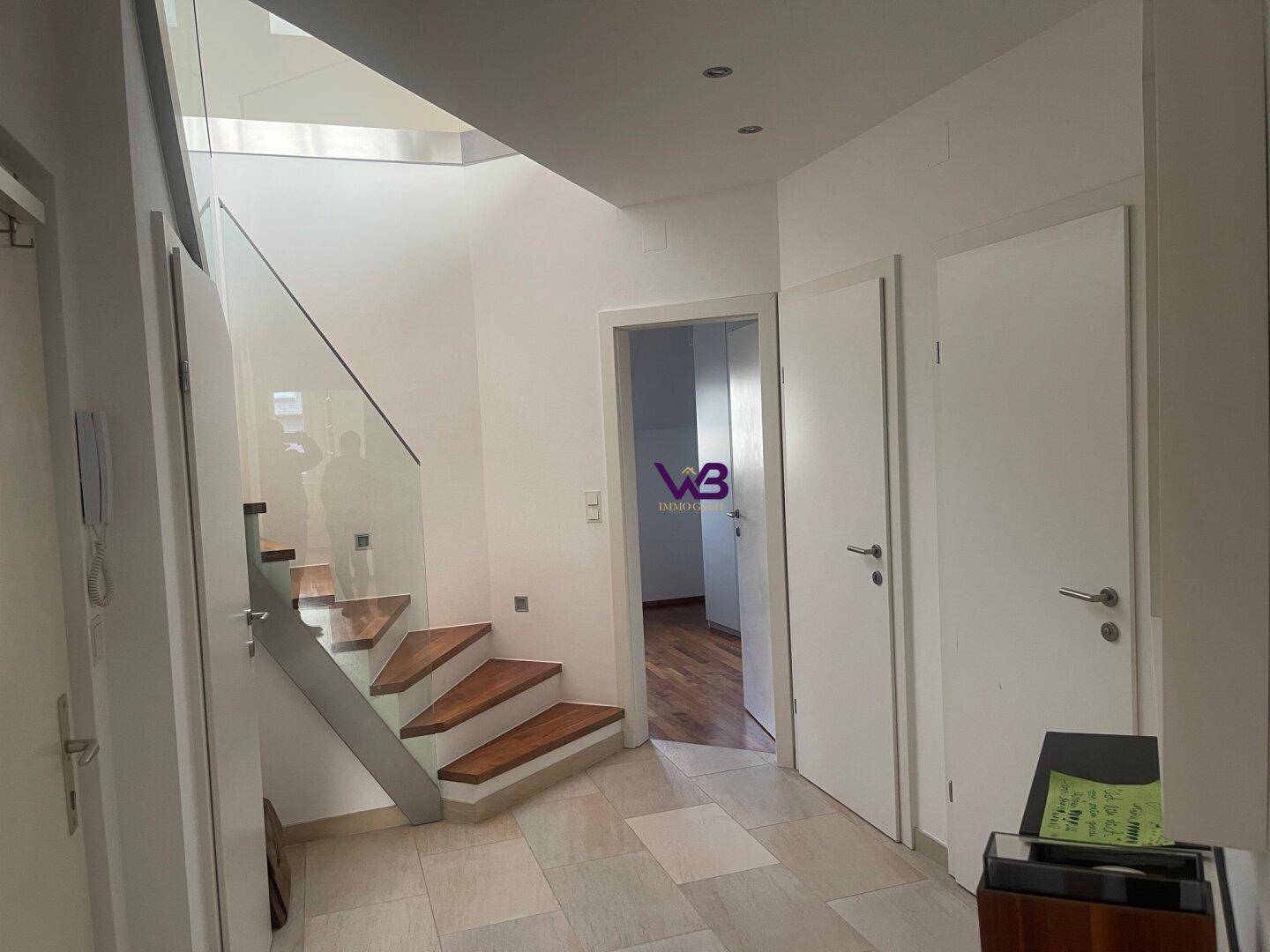 Heller Flur mit moderner Treppe aus Holz und Glas sowie Fliesenboden.