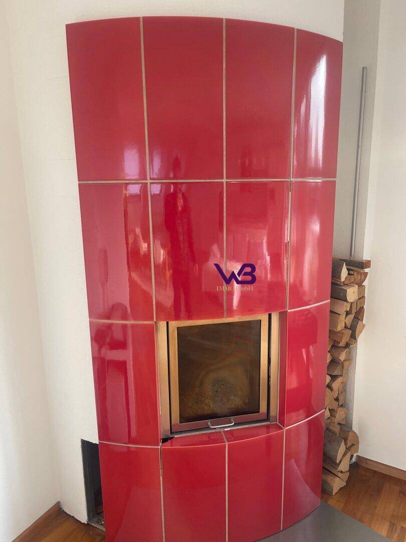 Nahaufnahme eines modernen roten Kachelofens mit sichtbarem Feuer und Holzscheiten.