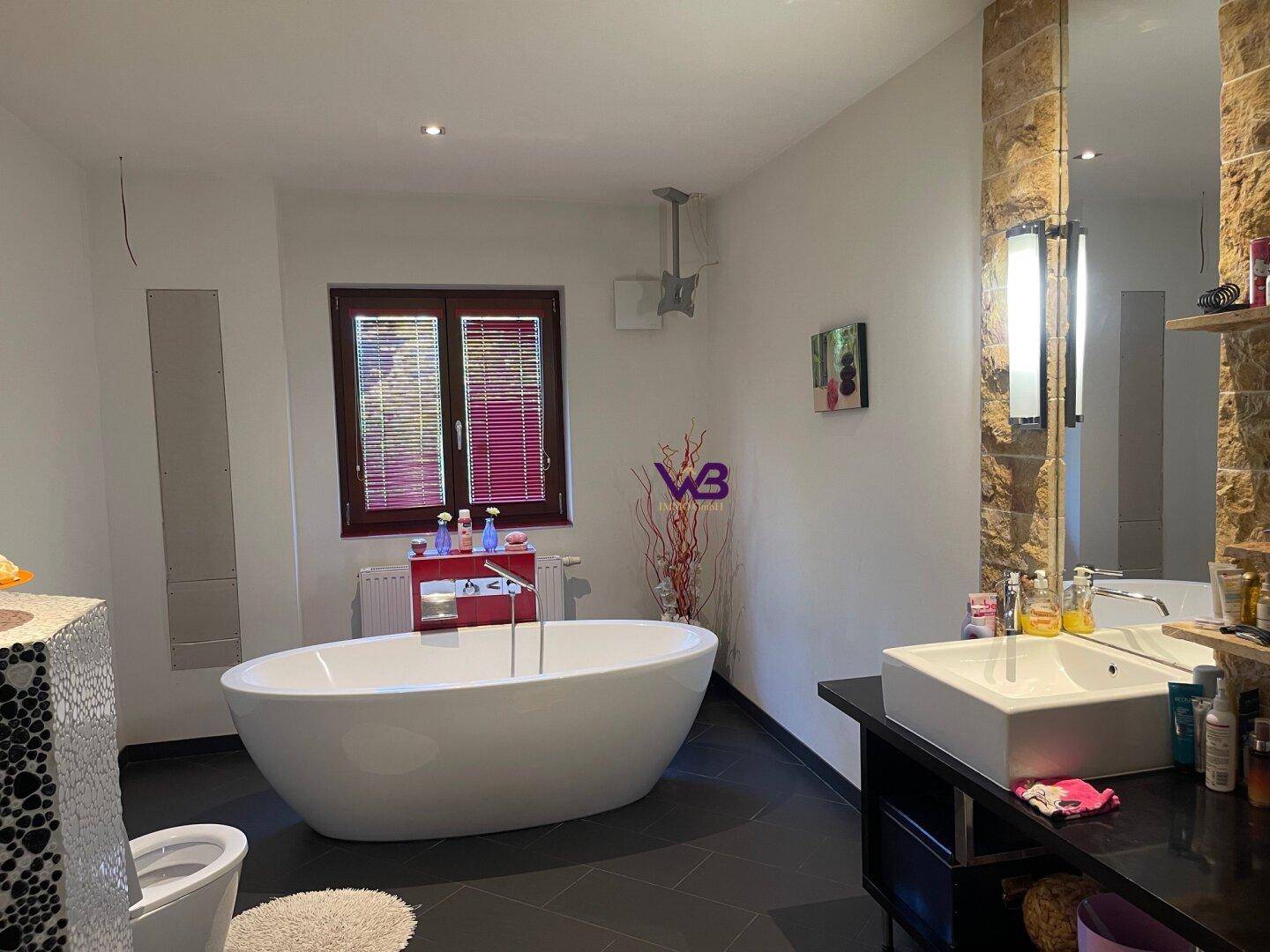 Geräumiges Badezimmer mit freistehender Badewanne, Doppelwaschbecken und Fenster.