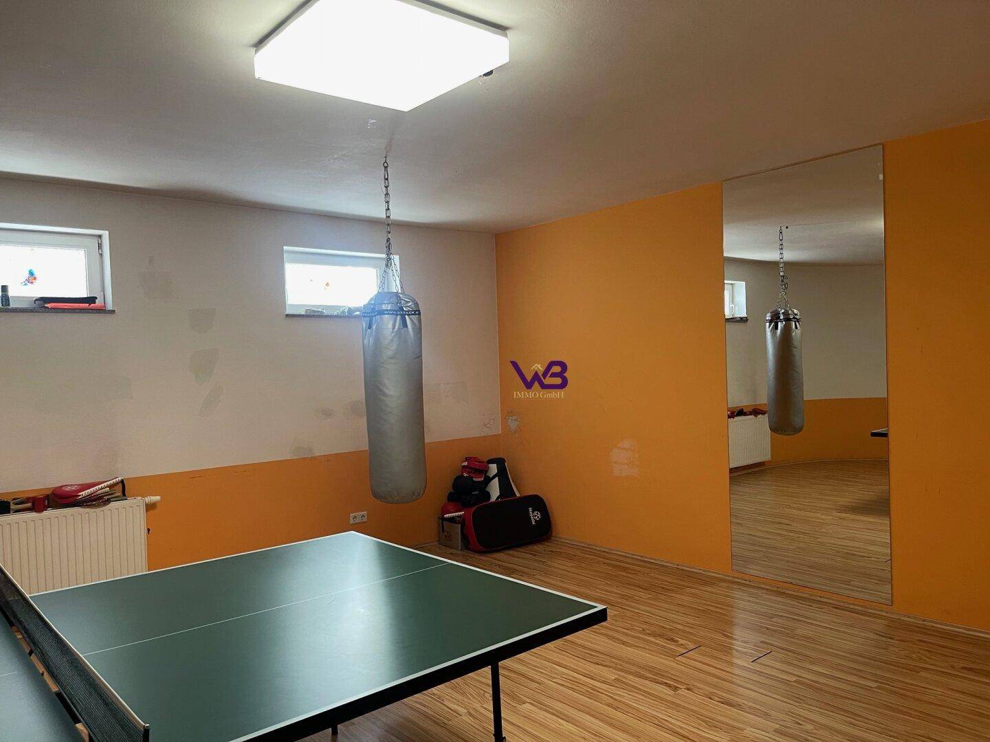 Fitnessraum mit Tischtennisplatte, Boxsack und Spiegelfläche für Training.