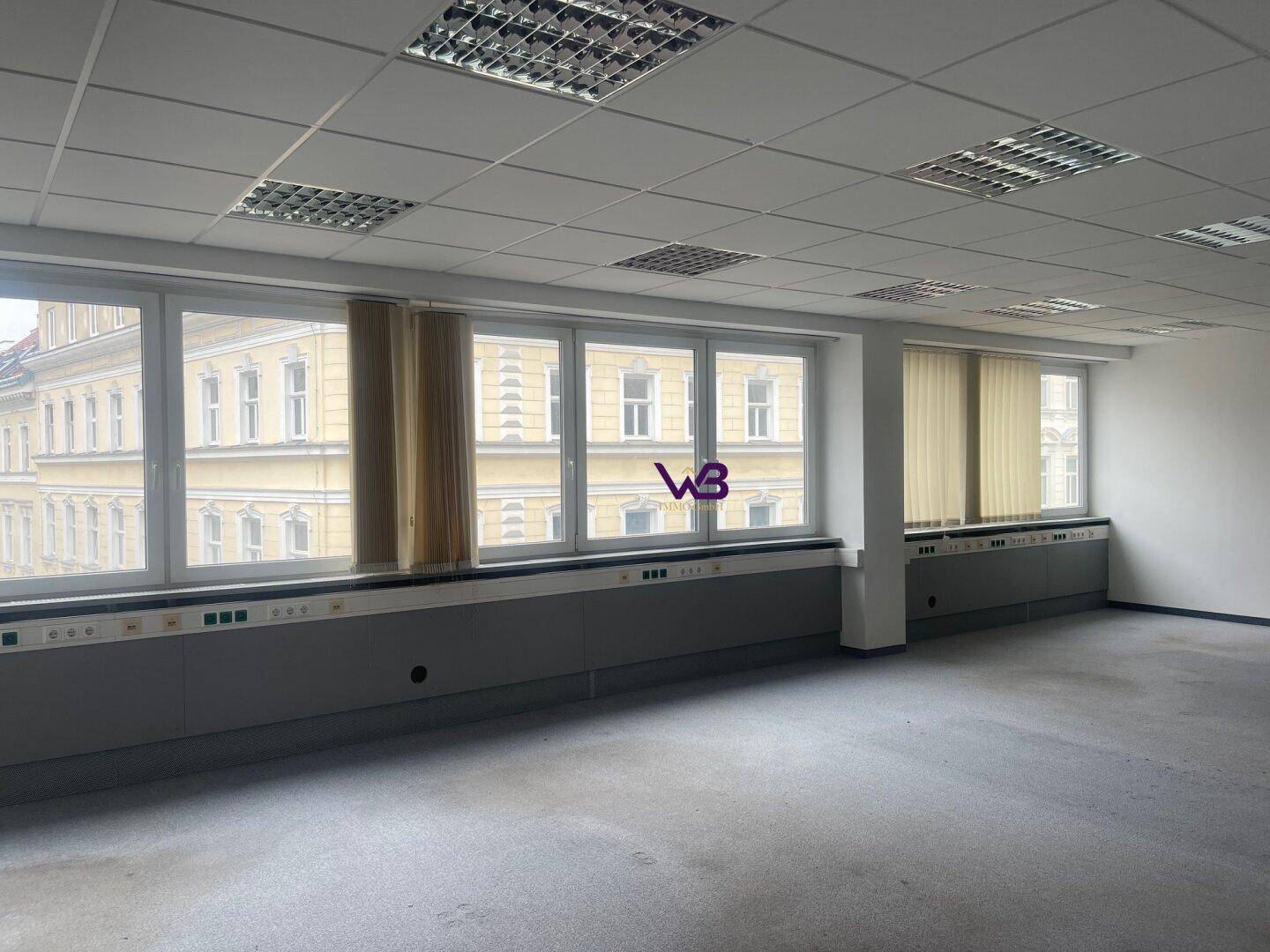 Großer Büroraum mit Teppichboden, vielen Fenstern und Deckenbeleuchtung, bietet viel Tageslicht.