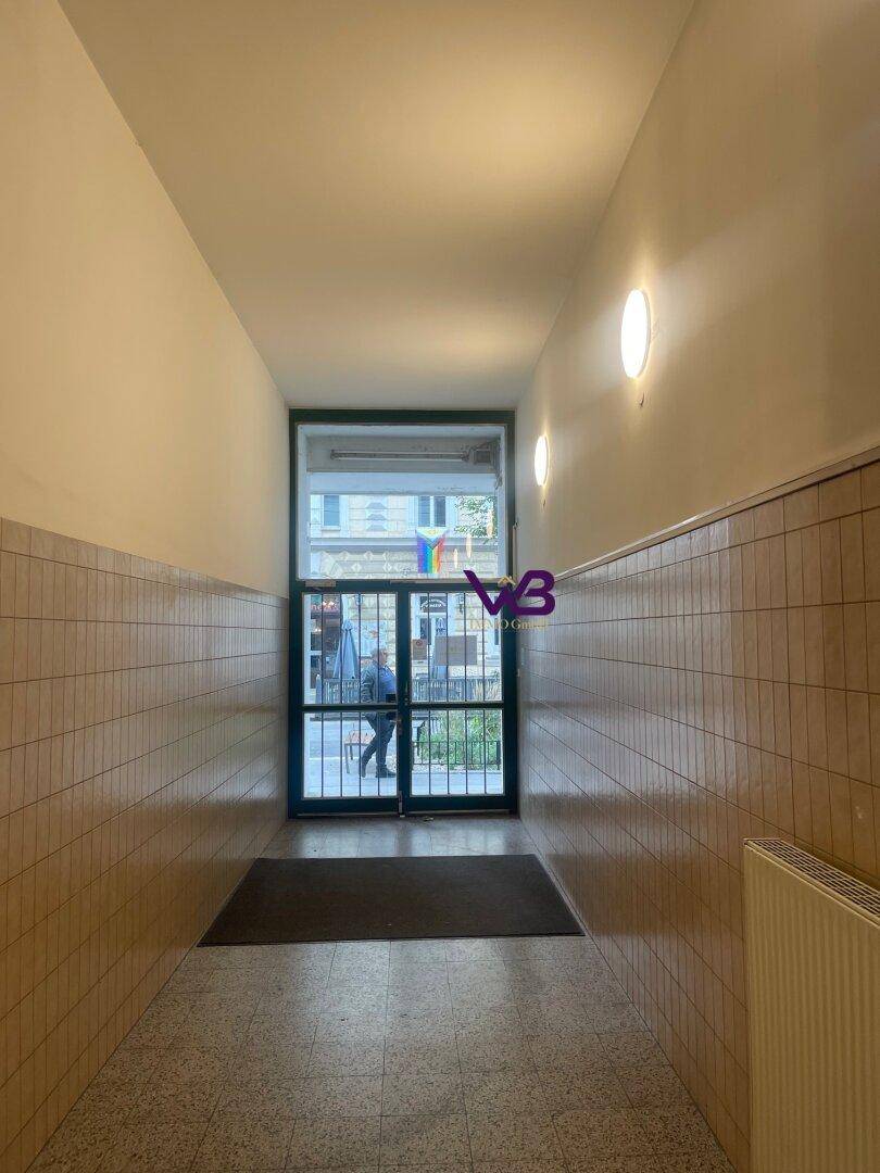 Langer Flur mit gefliestem Boden, hellen Wänden und einer Glastür zum Eingangsbereich.