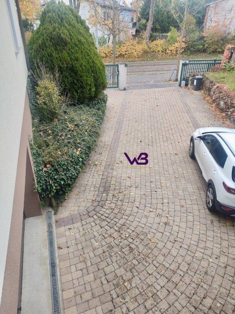 Gepflasterte Einfahrt mit Parkplatz für ein Fahrzeug, umgeben von grüner Bepflanzung.