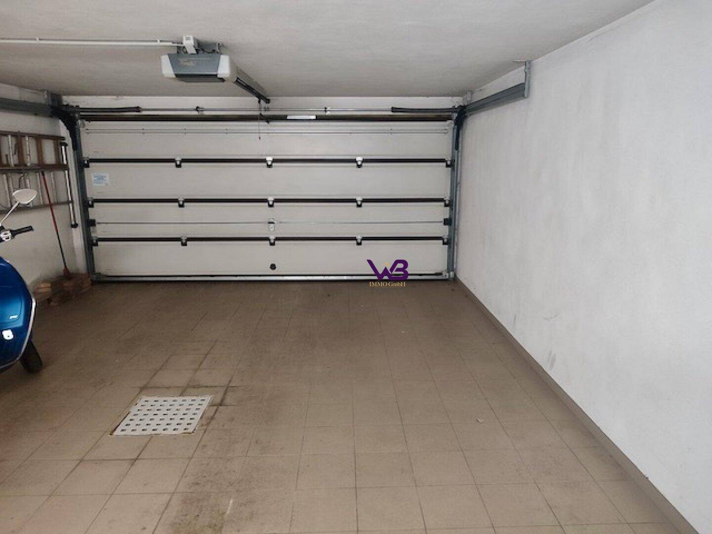 Geräumige Garage mit automatischem Tor und Fliesenboden, ideal für Fahrzeuge.