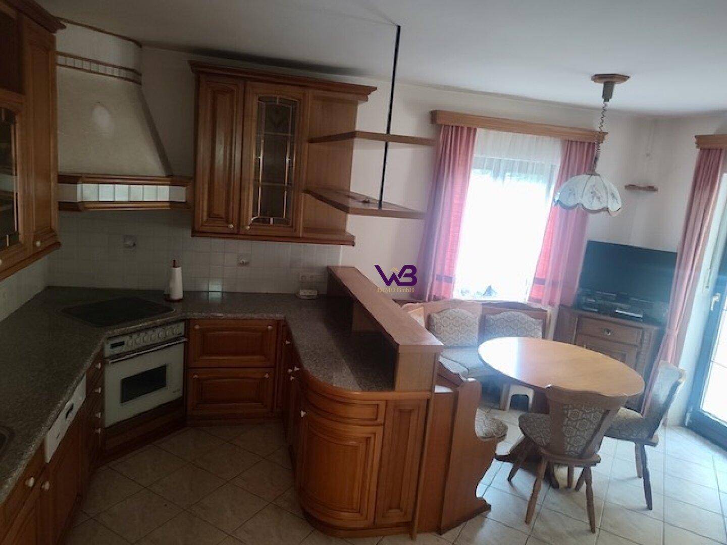 Traditionelle Küche mit Holzeinbauten, Essbereich und Fenster mit Vorhängen.